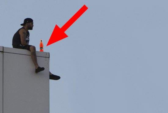 Un bărbat stă pe marginea unei clădiri cu un cidru în mână și amenință că îl bea