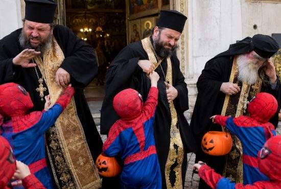 Oameni costumați în rochii negre cu aur, deranjați de copiii costumați în Spiderman de Halloween