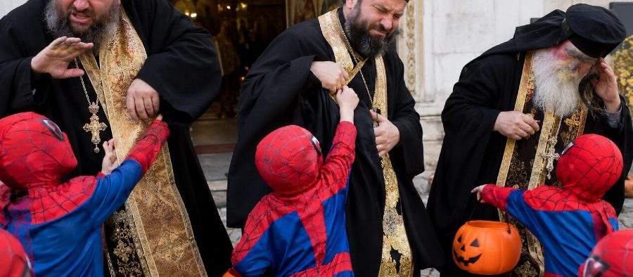 Oameni costumați în rochii negre cu aur, deranjați de copiii costumați în Spiderman de Halloween