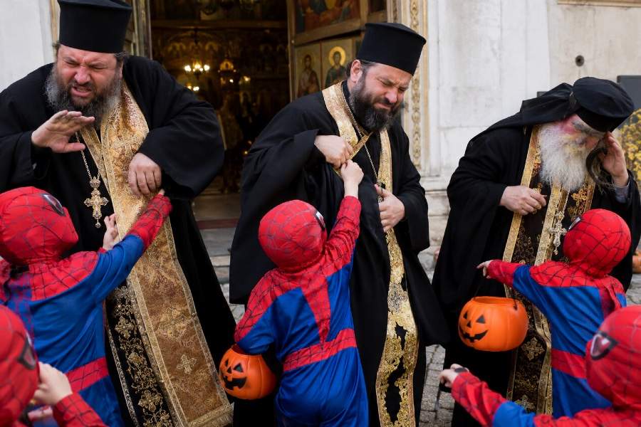 Oameni costumați în rochii negre cu aur, deranjați de copiii costumați în Spiderman de Halloween